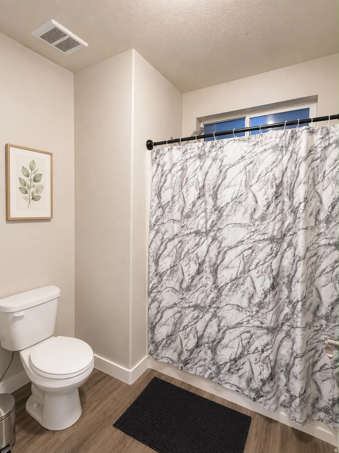 Bathroom featuring wood-finish flooring, a white toilet, and a window above the shower area