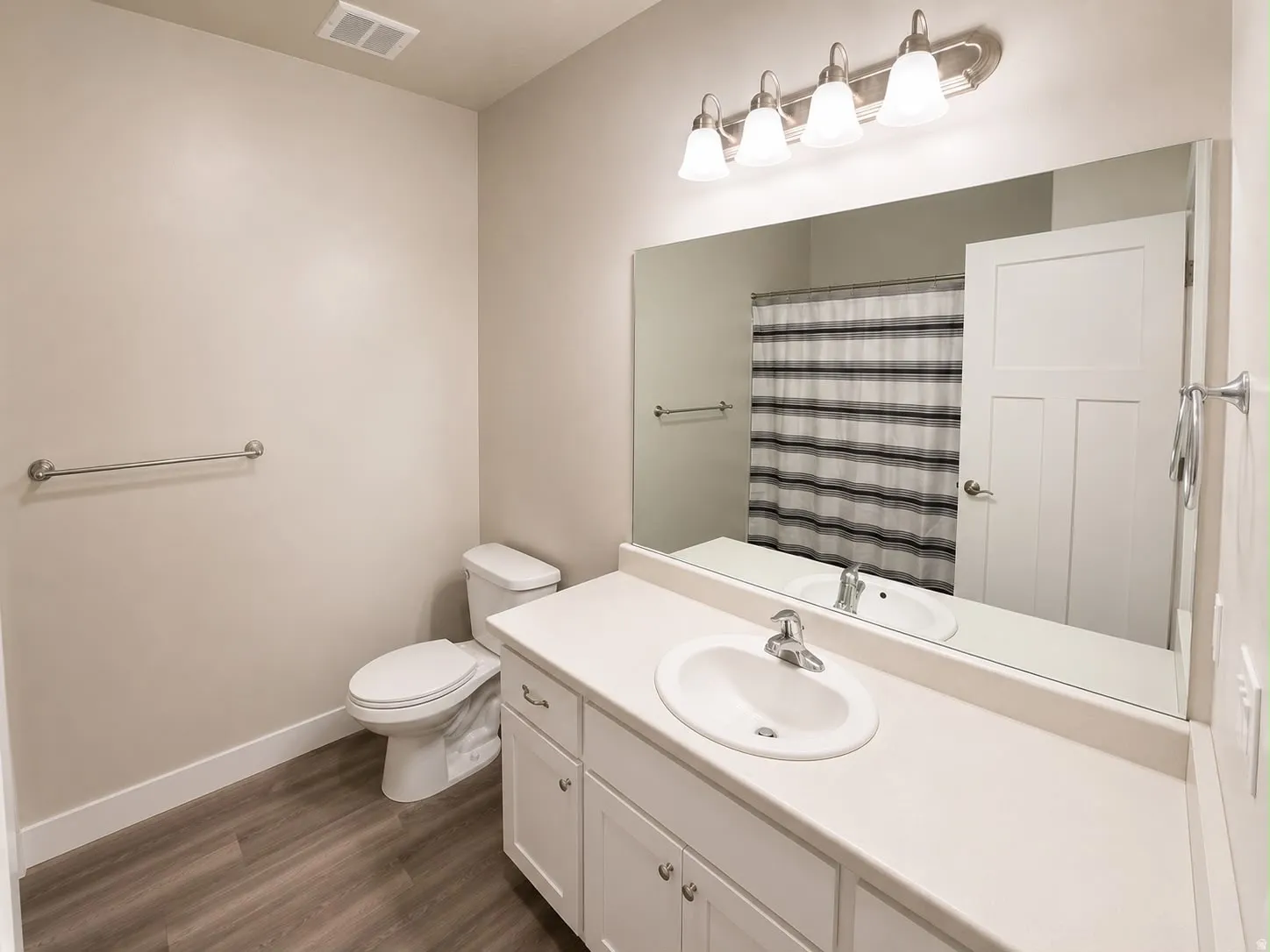 Bathroom featuring wood-finish flooring, a white vanity with an integrated sink, a large wall-mounted mirror, and a four-light fixture