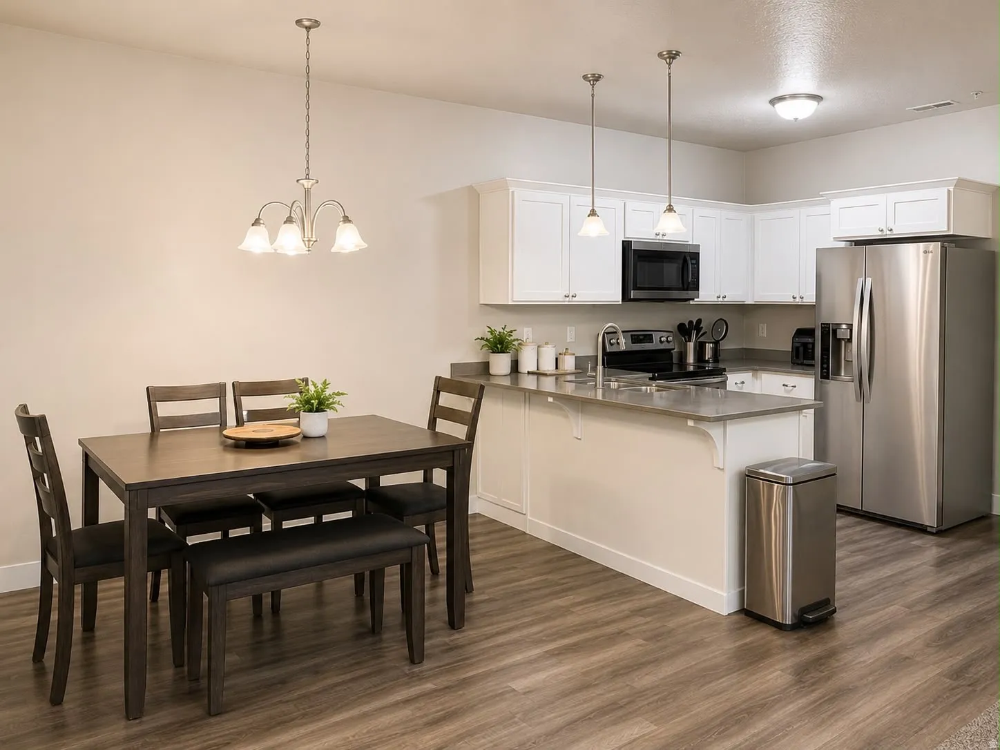 Open-concept kitchen and dining area featuring wood-finish flooring, white cabinetry, stainless steel appliances, and a peninsula with a composite countertop
