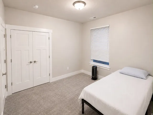 Neutral-toned room featuring a window with blinds, light gray textured carpeting, and white trim
