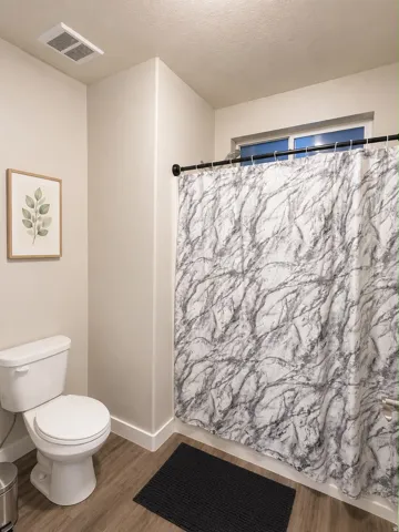 Bathroom featuring wood-finish flooring, a white toilet, and a window above the shower area
