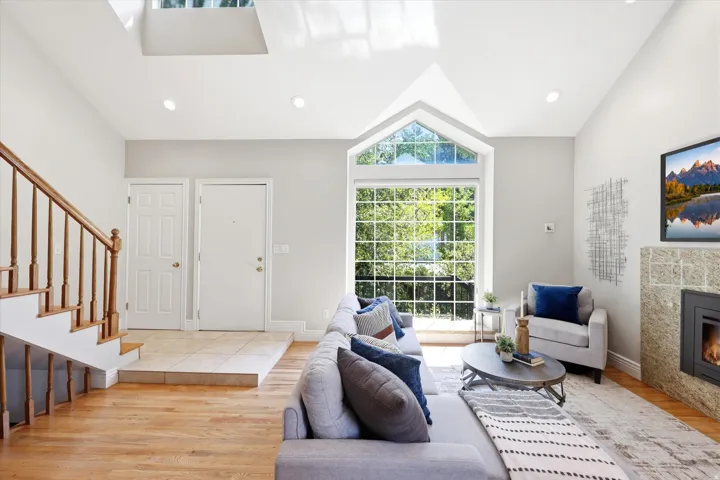 Living area featuring vaulted ceilings, a large picture window with an arched transom, wood-finish flooring, a stone-clad fireplace, and recessed lighting