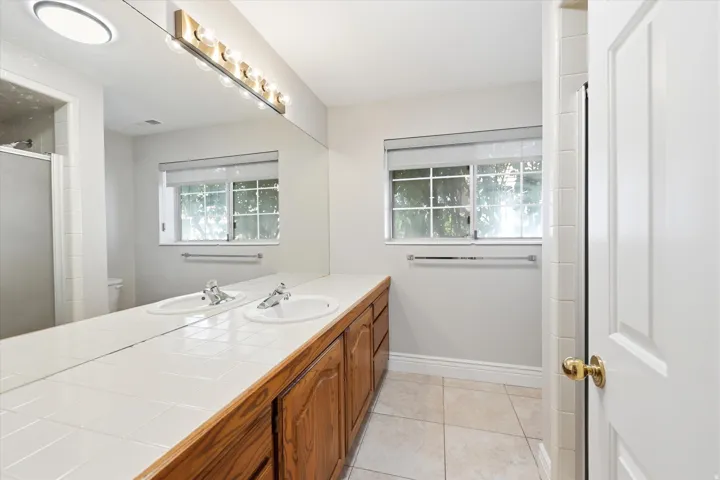 Double vanity featuring integrated sinks, tile countertop, and wood-finish cabinetry