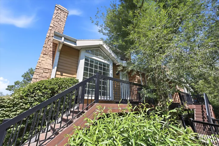 Exterior featuring a prominent stone chimney, multi-level wood-look decking, and black metal railings