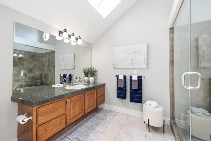 Bathroom featuring a wood-finish double vanity with a dark countertop, dual undermount sinks, and a full-width mirror