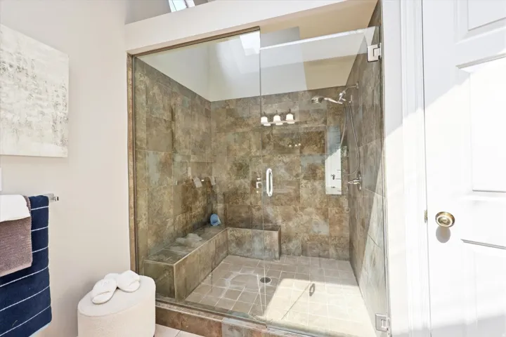 Glass-enclosed shower featuring full-height tile, built-in benches, a skylight, and a rainfall showerhead with additional handheld spray