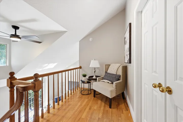 Hardwood flooring extending through the upper hall with a wood banister, white walls, white doors with brass hardware, and a ceiling fan
