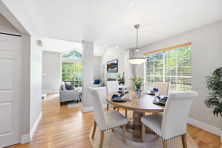 Dining area with wood-finish flooring, a contemporary chandelier, and a large window with blinds