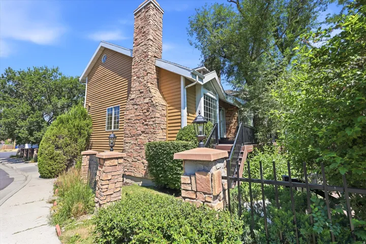 Exterior featuring horizontal siding, a prominent stone chimney, and a decorative wrought iron fence