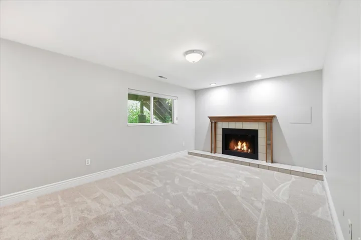 Spacious room featuring a fireplace with a wood mantle and tile surround, recessed lighting, and light-colored carpet flooring