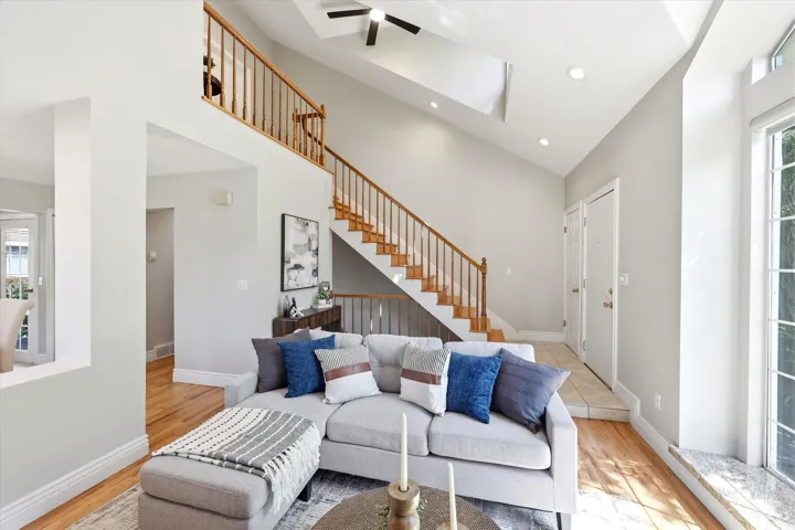 Vaulted ceiling living area featuring wood-finish flooring, a contemporary ceiling fan, and a prominent staircase with wood railings and treads