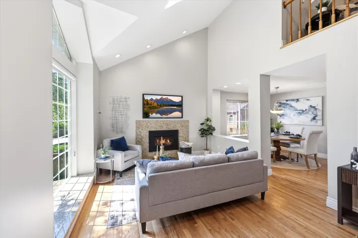 Vaulted living area featuring a fireplace with stone surround, hardwood flooring, and large windows with transom architectural details