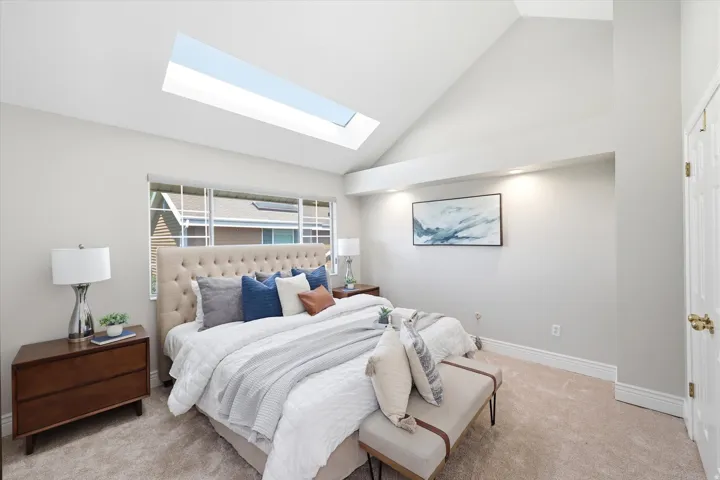 Vaulted ceiling room featuring a skylight, broad window with white trim, recessed wall niche with accent lighting, and plush carpeting
