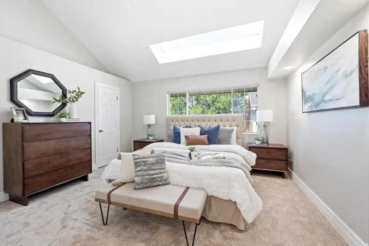 Vaulted ceiling bedroom featuring a skylight, window with exterior greenery, and plush carpeting