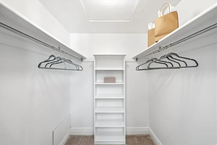 Walk-in closet featuring built-in shelving, dual hanging rods, and an overhead access panel