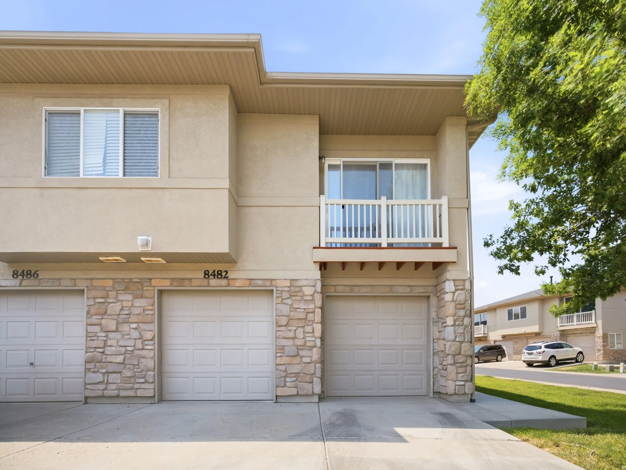 Exterior featuring a balcony with white railings, a stucco finish, stone accents, two garage doors, and a concrete driveway