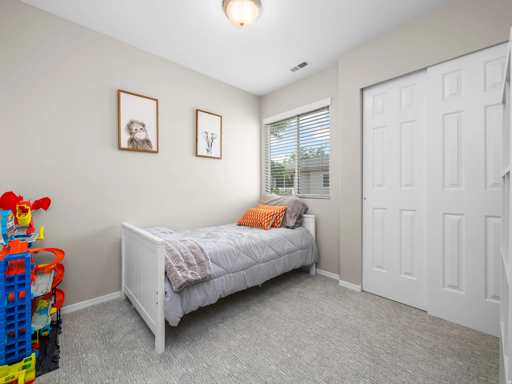 Bedroom featuring light gray walls, textured gray carpeting, a window with blinds, and white bi-fold closet doors