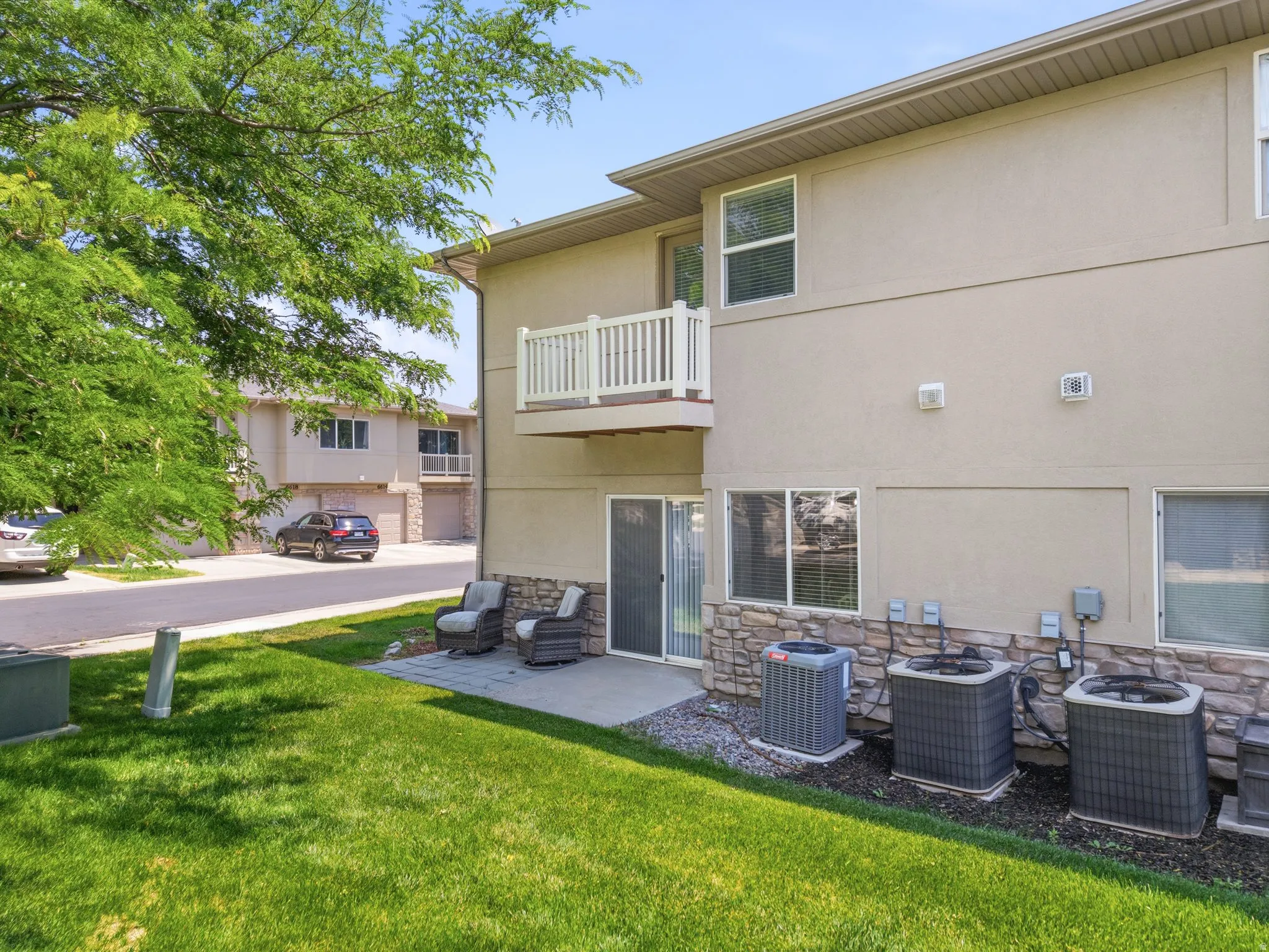 Rear exterior featuring a ground-level patio, upper-level balcony with white railings, and a stone-clad foundation