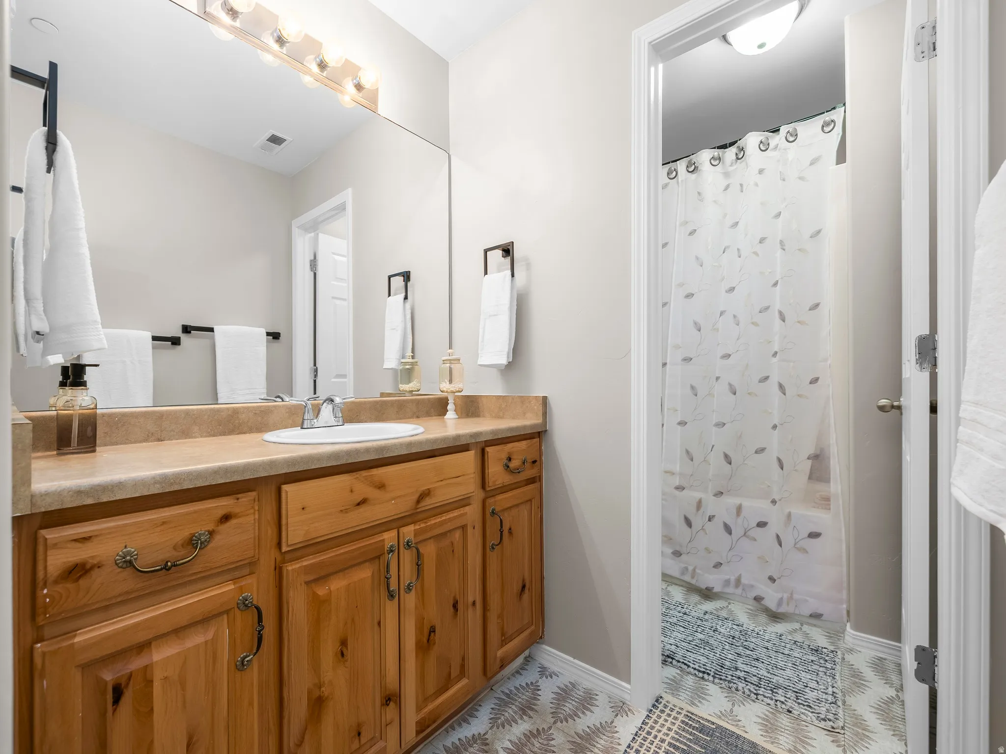 Bathroom vanity featuring a single basin, light wood cabinetry with brass-toned hardware, and a laminate countertop