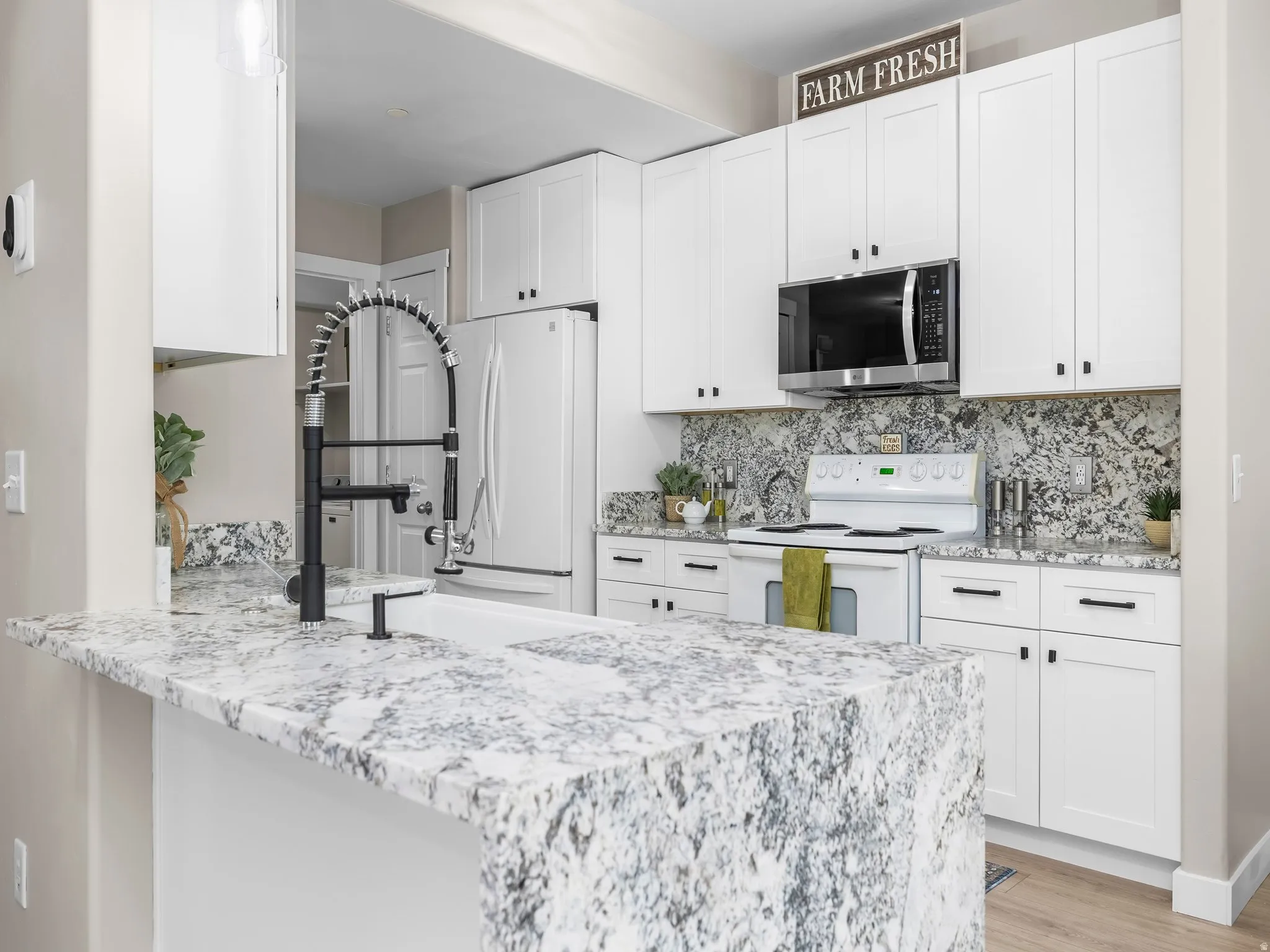 Contemporary kitchen featuring white cabinetry, a large kitchen island with a waterfall countertop, a black pull-down faucet, a built-in microwave, and matching stone countertops and backsplash