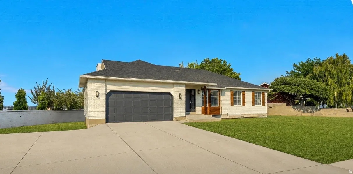 Ranch-style exterior featuring a dark gray garage door, white brick facade, and a dark shingle roof