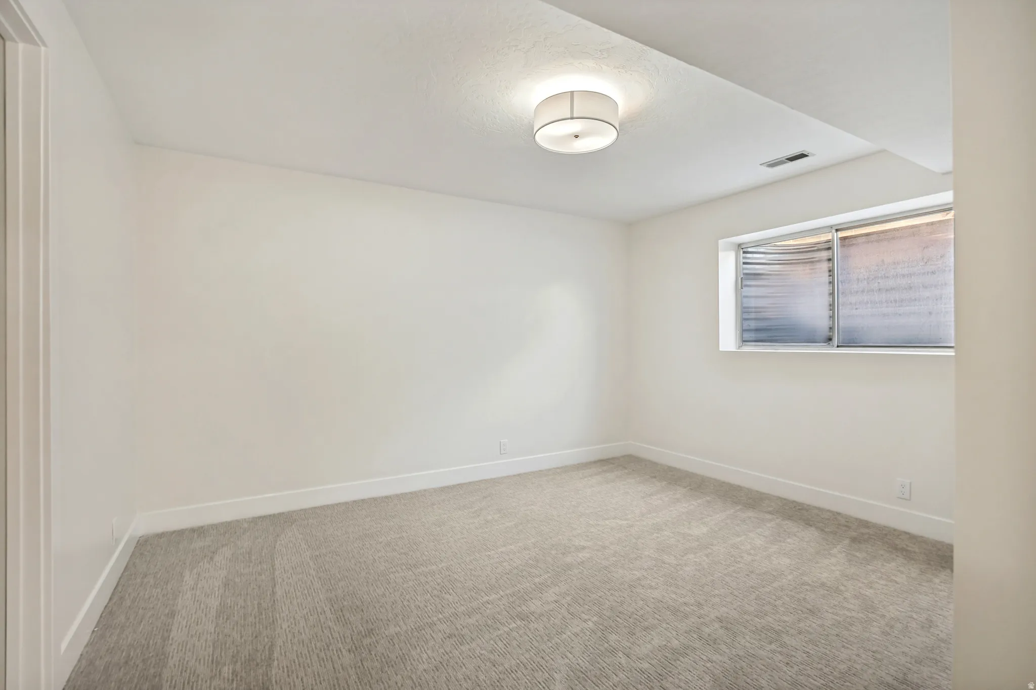 Room featuring light-toned carpeting, white walls, and a single window with blinds