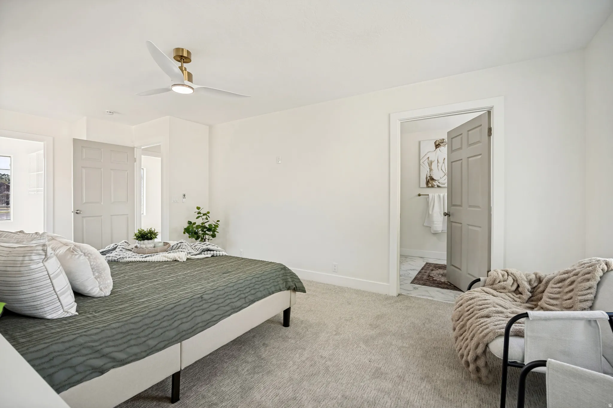 Spacious room with light neutral wall tones, plush carpet flooring, a modern ceiling fan with integrated lighting, and a doorway revealing a bathroom with tile flooring
