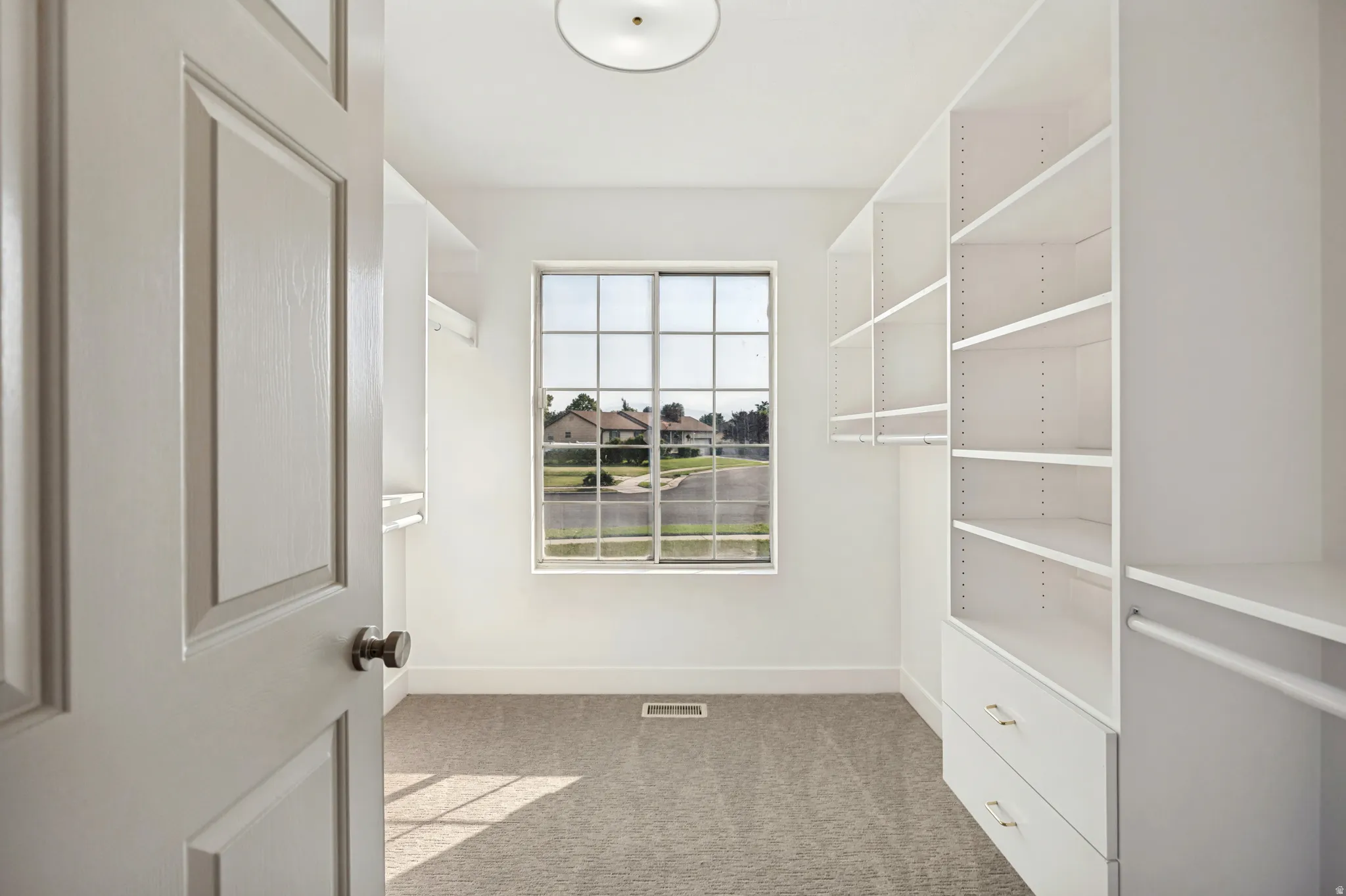 Walk-in closet with built-in shelving, integrated drawers, hanging rods, and a large window