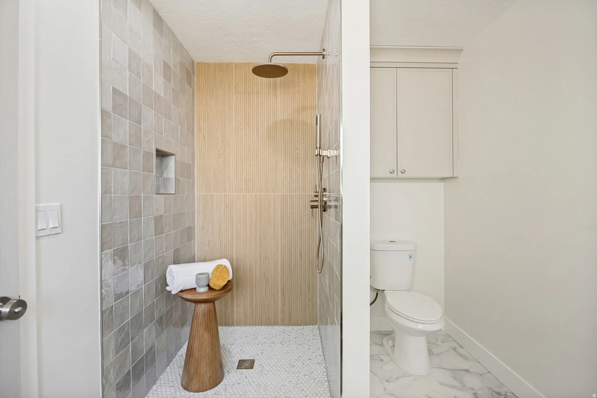 Walk-in shower featuring light-toned square wall tiles, a recessed niche, a rain showerhead, and small hexagonal floor tiles