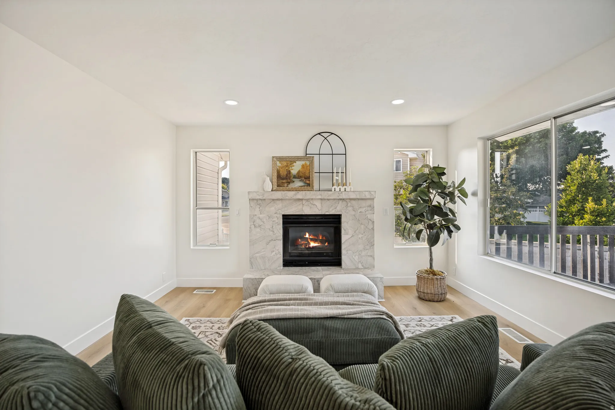 Living area featuring a stone-surround fireplace, wood-finish flooring, white walls, recessed lighting, and large windows