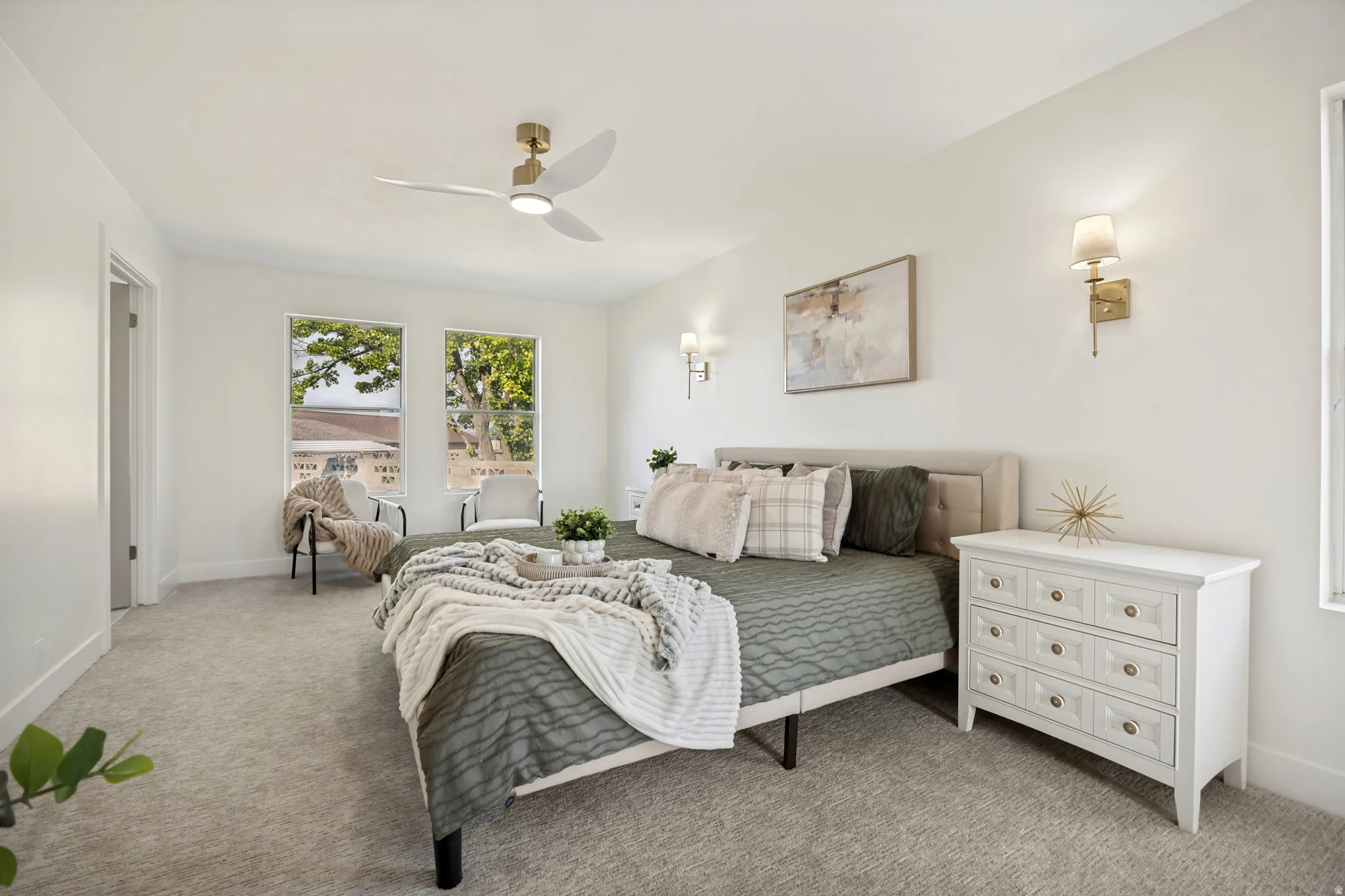Carpeted bedroom featuring a contemporary gold-finish ceiling fan with integrated lighting, a pair of rectangular windows, and dual wall sconces