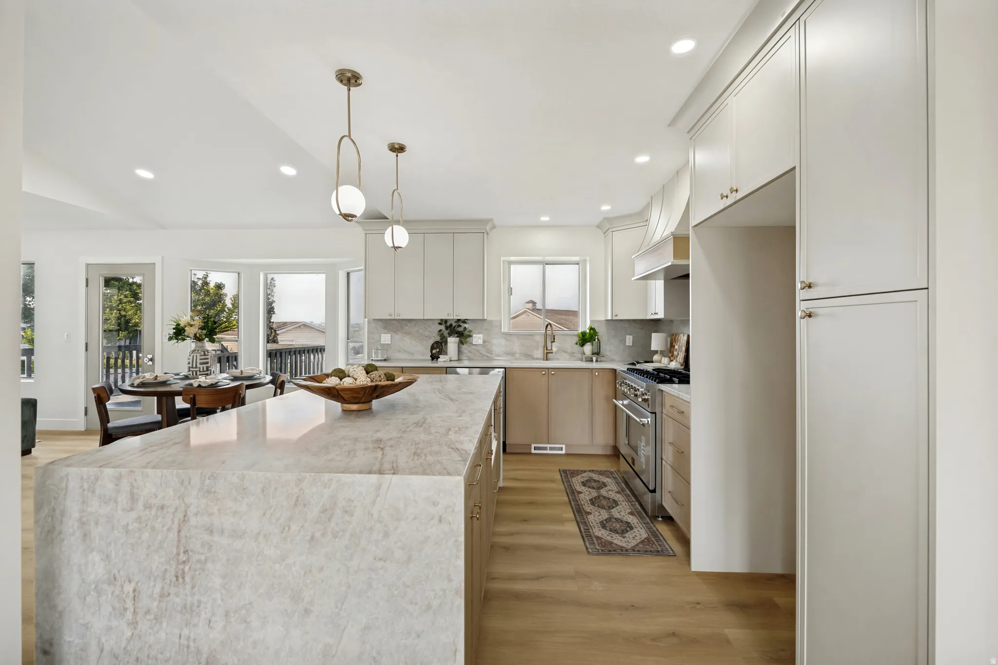 Expansive kitchen featuring a large stone-finish island with waterfall edge, full-height cabinetry, stainless steel range, and wood-finish flooring