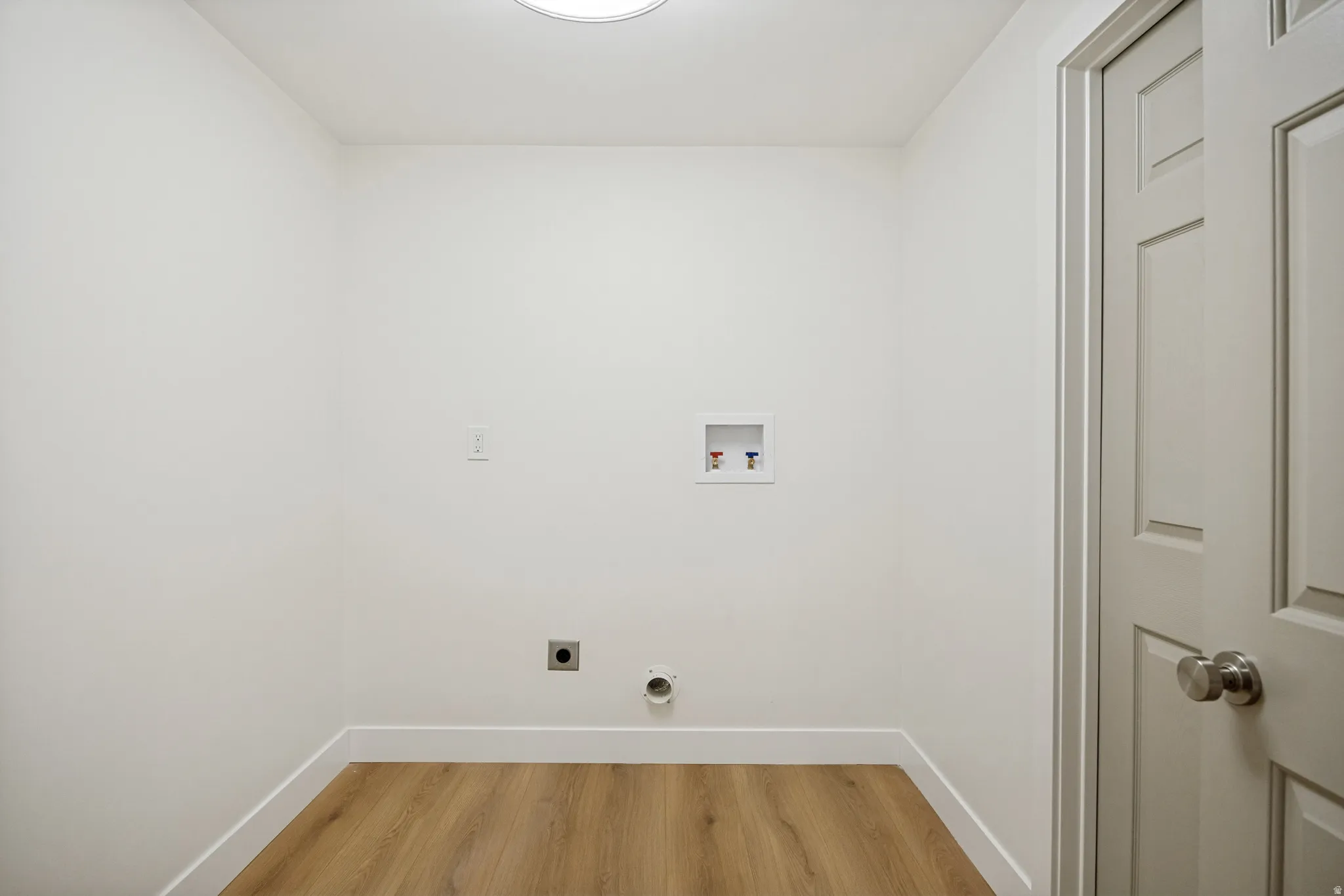 Dedicated laundry area featuring wood-finish flooring, white baseboards, and a paneled door with brushed nickel hardware