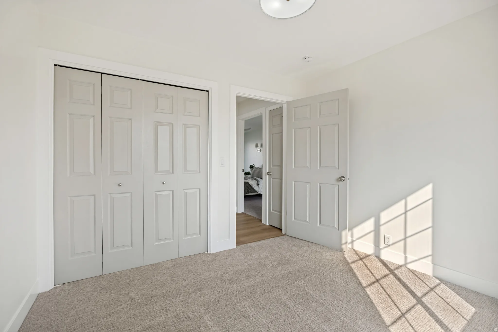 Neutral tone carpeting and white walls in a room featuring a bi-fold closet with panel doors and a six-panel interior door