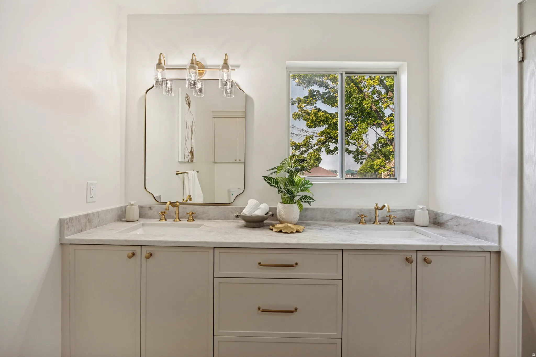 Dual vanity with light-toned cabinetry, integrated sinks, brass-finish fixtures, and a coordinating mirror