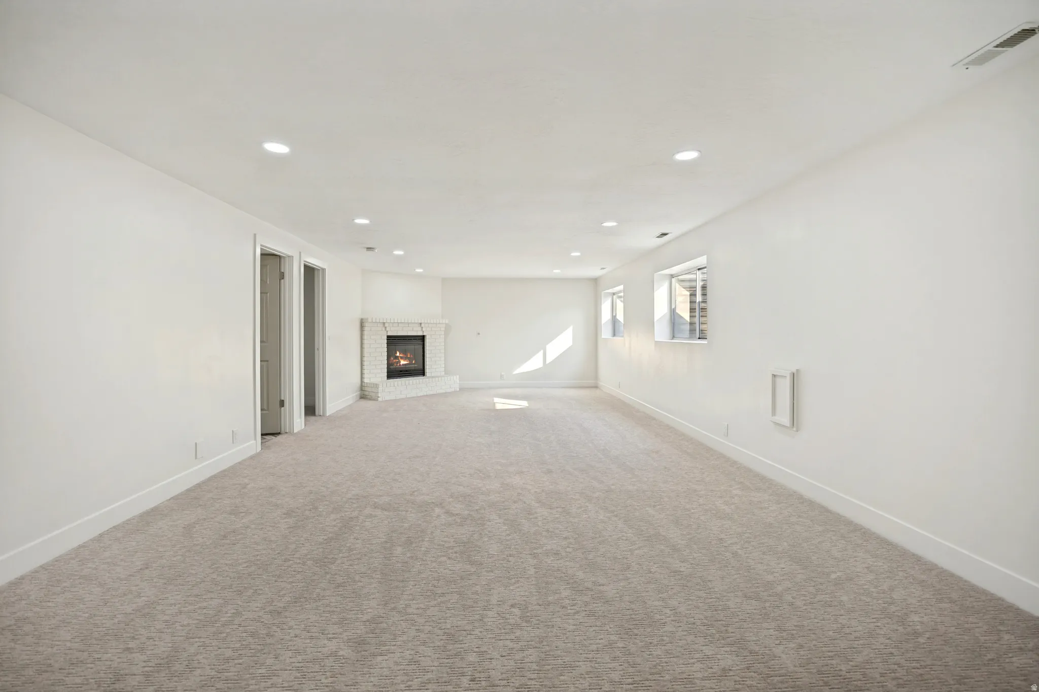 Spacious room featuring neutral carpeting, a corner brick fireplace, recessed lighting, and white walls with baseboards