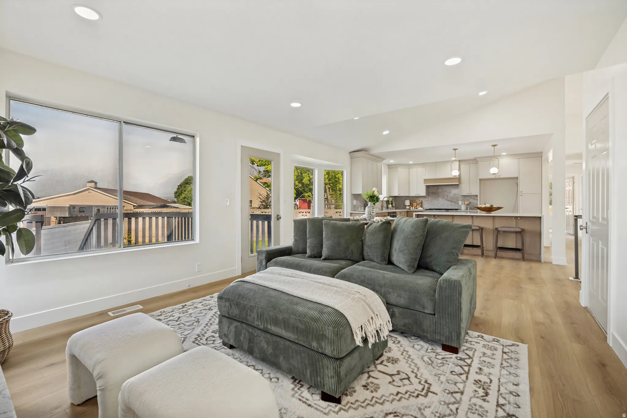 Vaulted ceiling interior featuring wood-finish flooring, recessed lighting, and a kitchen visible from the living area