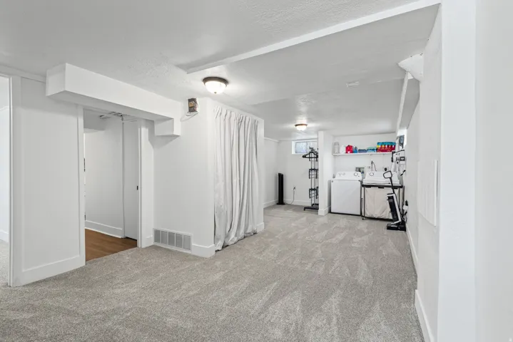 Spacious carpeted room featuring a dedicated laundry area with a utility sink, washer, and dryer