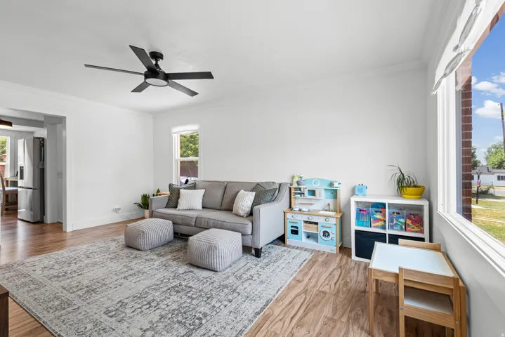 Living area featuring wood-finish flooring, white walls, crown molding, and a contemporary ceiling fan