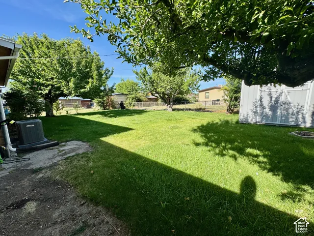 Spacious rear yard with a verdant lawn, mature trees providing shade, and a detached storage shed
