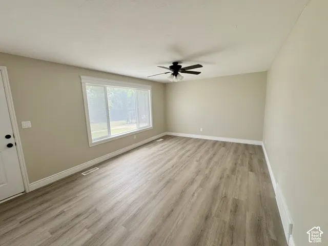 Spacious room featuring wood-finish flooring, a large window with white trim, and a ceiling fan with light fixture