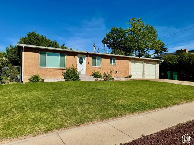 Brick exterior featuring a two-car garage, mature front lawn, and concrete driveway