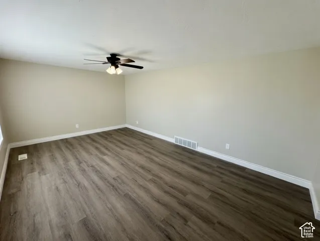 Spacious room featuring wood-finish flooring, light neutral wall tones, white baseboards, and a ceiling fan with integrated lighting