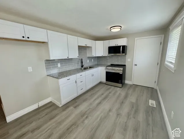 Kitchen featuring white shaker cabinetry, gray subway tile backsplash, granite countertops, and stainless steel appliances