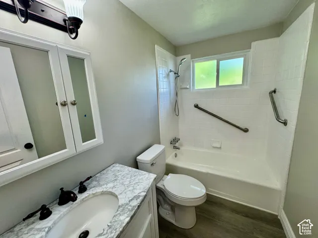 Bathroom featuring a single vanity with stone-finish countertop, white cabinetry with mirrored medicine cabinet, a full bathtub with white subway tile surround, and wood-finish flooring