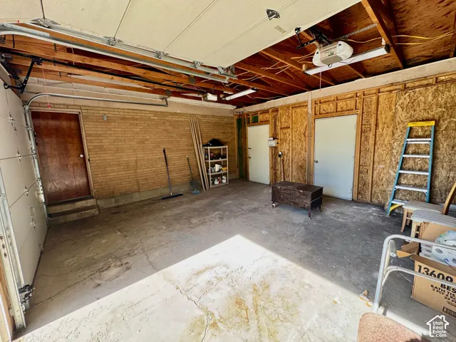 Spacious garage featuring a concrete floor, exposed wood beam ceiling, automatic garage door opener, brick wall, and two interior access doors