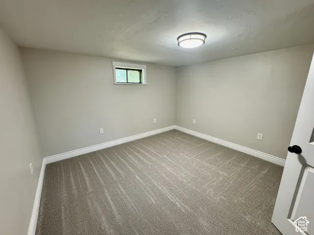 Interior room featuring light gray walls, patterned gray carpet, white baseboards, and a single window with white trim