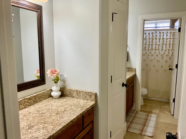 Bathroom featuring granite countertops, wood cabinetry, a decorative framed mirror, and tile flooring