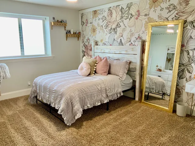 Bedroom featuring floral accent wall, light-colored walls, and textured carpeting