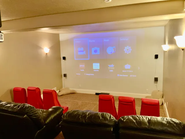 Dedicated media room featuring a large projection screen, wall-mounted speakers, and integrated wall sconce lighting